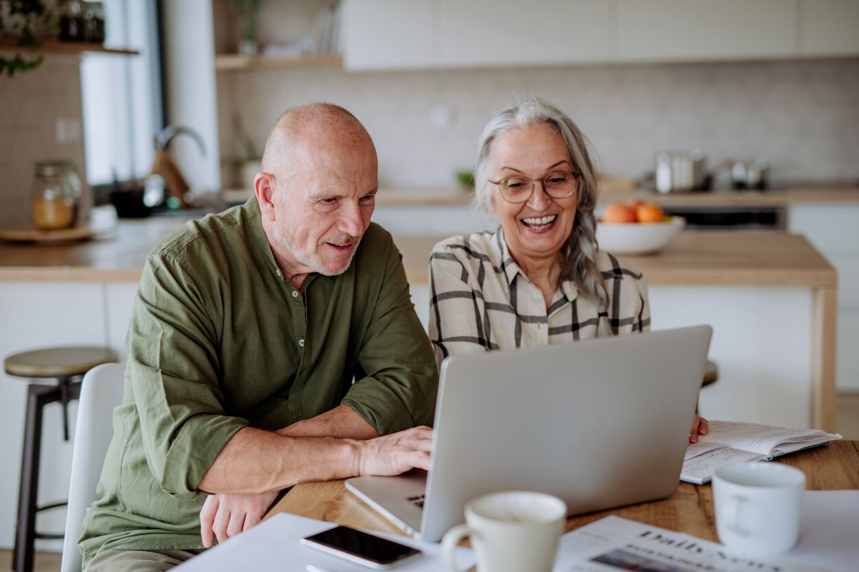 A happy senior couple calculates expenses or planning budget together at home.