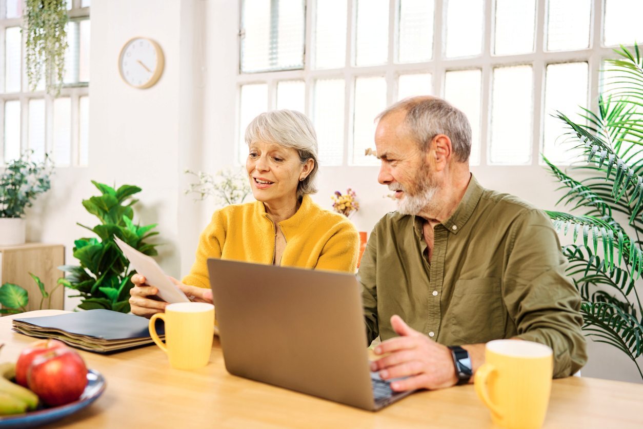 Senior couple managing finances with a laptop and documents at home.